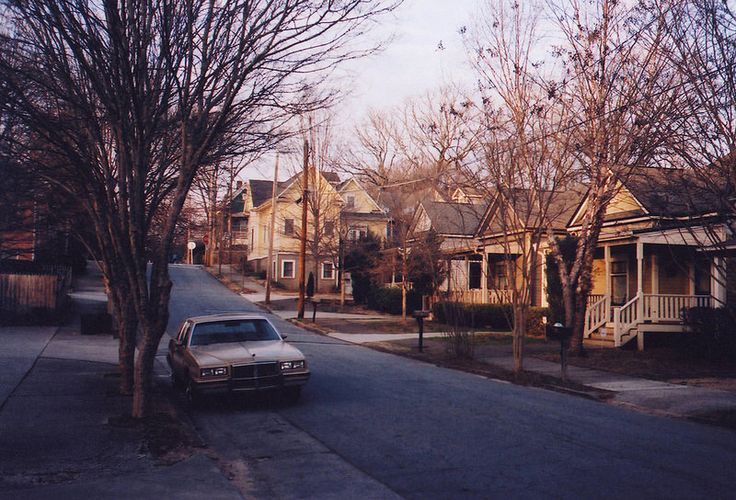 a car parked on the side of a street next to trees and houses with no leaves