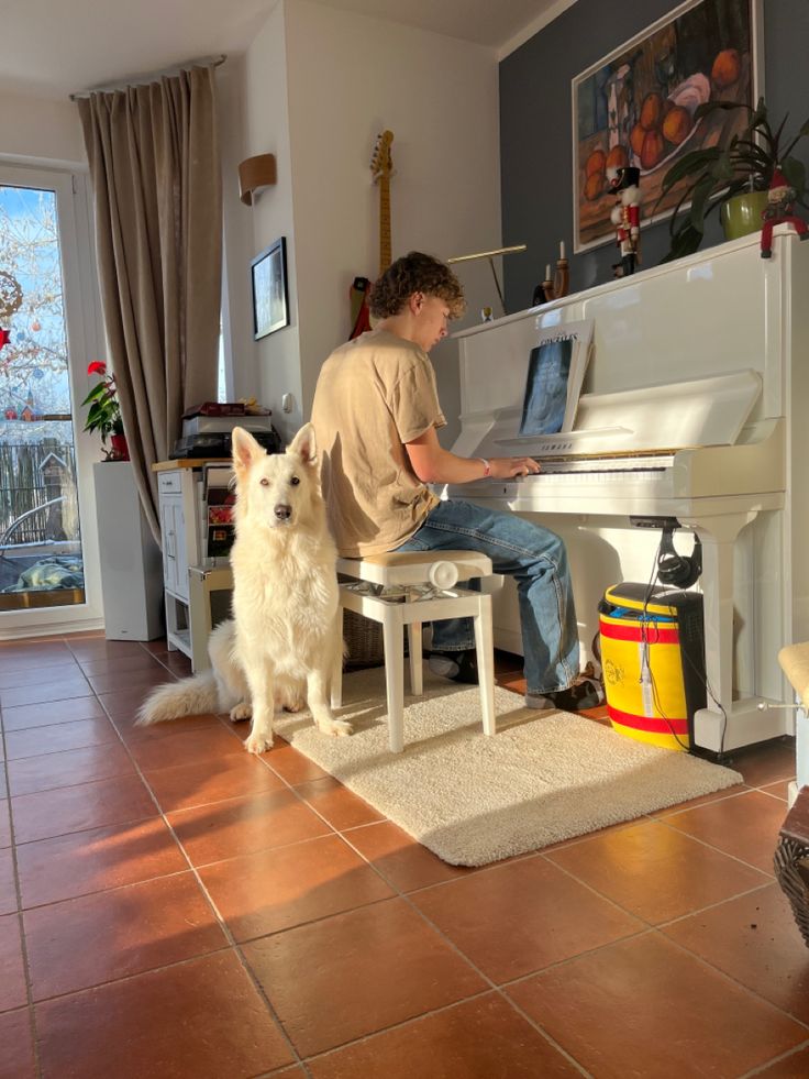 a man sitting at a white piano with his dog standing next to him in front of it