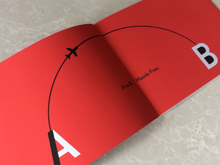 an open red book with black and white letters on the cover, which is shaped like a plane