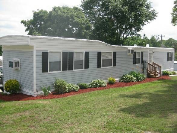 a mobile home sits in the middle of a grassy area with trees and bushes around it