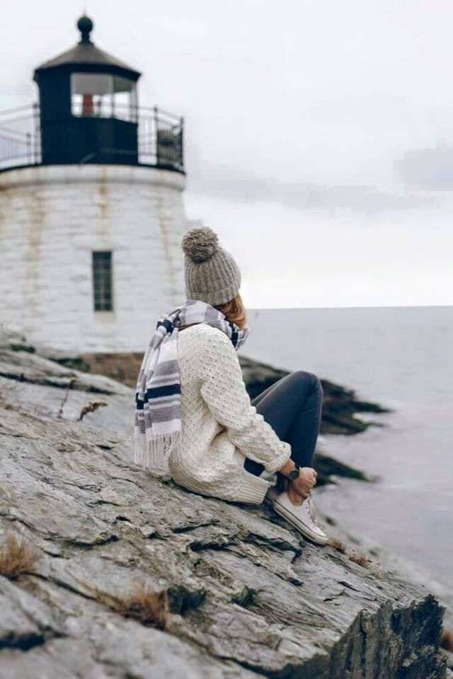 a woman sitting on top of a rock next to the ocean near a light house