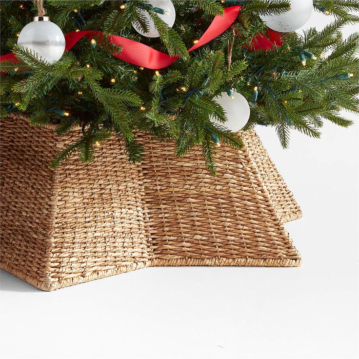 a christmas tree in a wicker basket with red ribbon and ornaments on the top