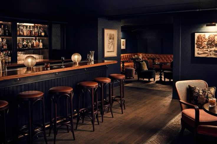 a dimly lit bar with stools and wooden tables in the corner, along with pictures on the wall