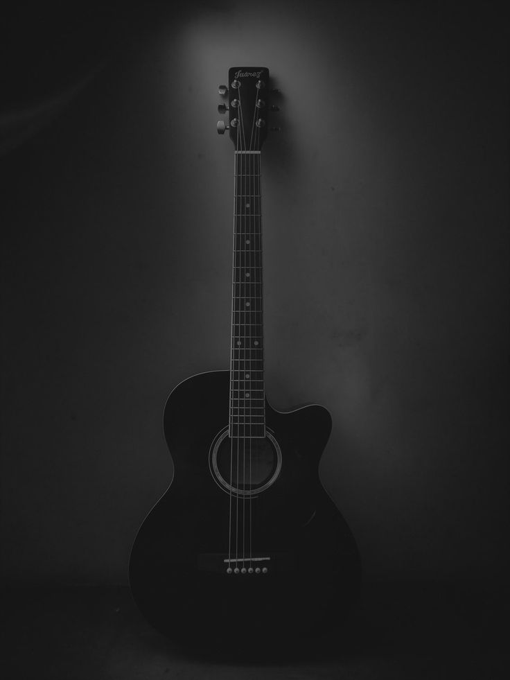 a black and white photo of an acoustic guitar against a dark background with the light on