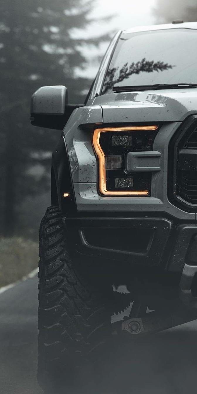 the front end of a gray truck driving down a road with trees in the background