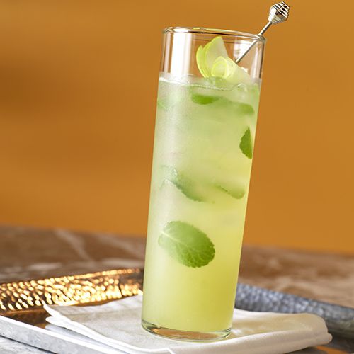 a tall glass filled with limeade on top of a table next to a knife