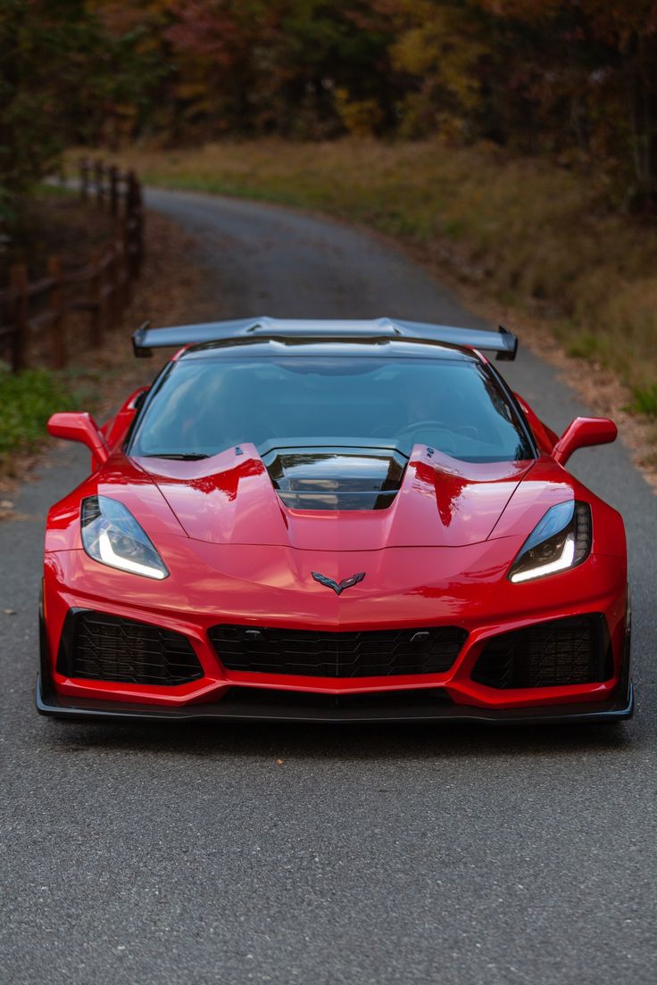 a red sports car parked on the side of a road next to a wooded area