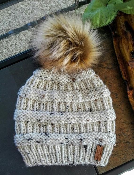 a white knitted hat with a brown pom - pom sitting on top of it