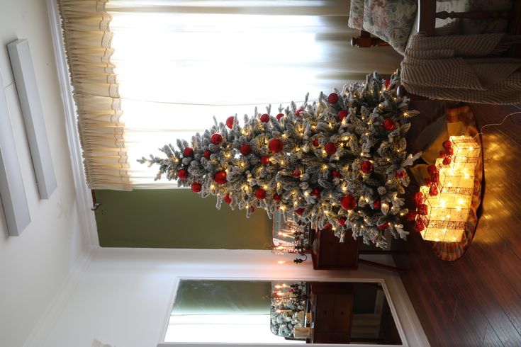 a lit christmas tree in a living room next to a window with curtains on the windowsill