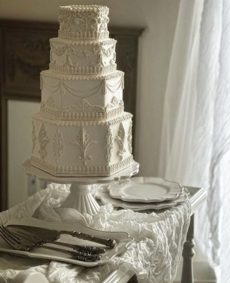 a white wedding cake sitting on top of a table next to silverware and utensils