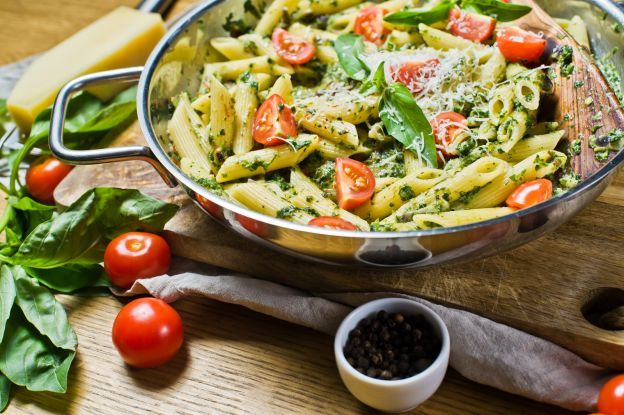 a pan filled with pasta and vegetables on top of a wooden cutting board