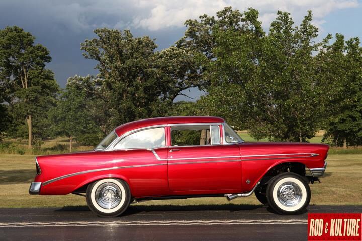 an old red car is parked on the side of the road in front of some trees