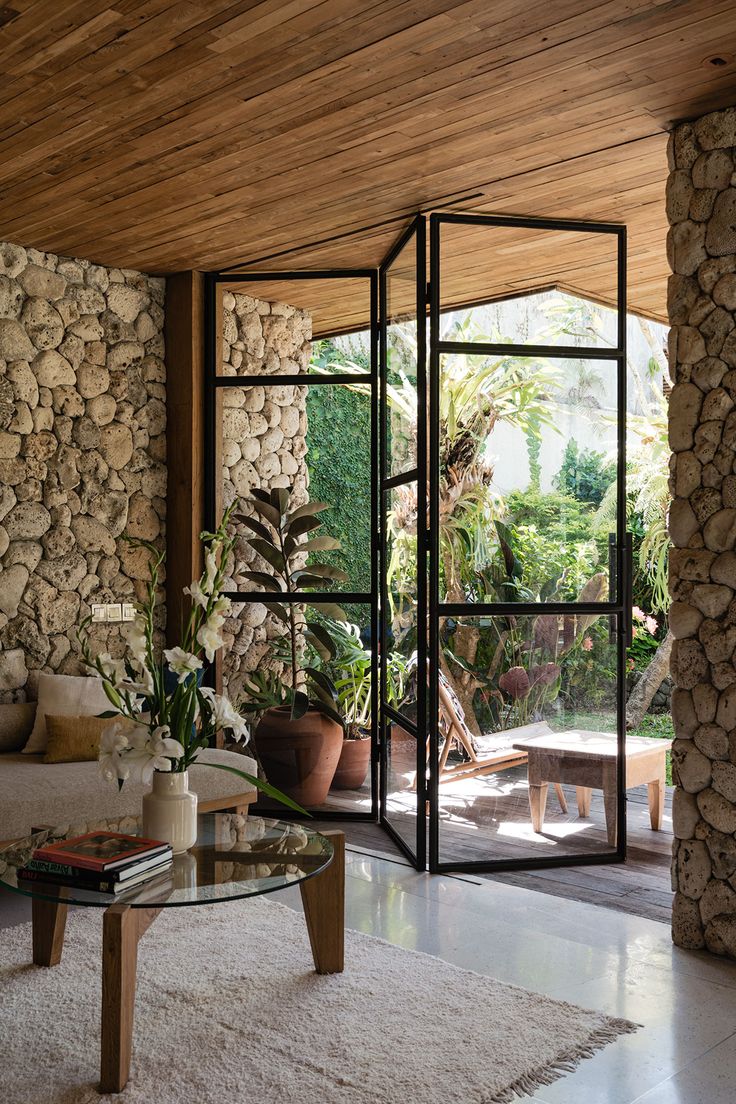 a living room filled with furniture and a stone wall next to a window covered in plants