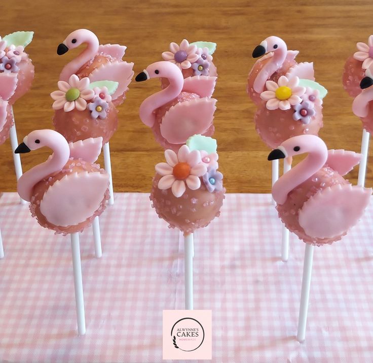 pink flamingo lollipops with flowers on them sitting on top of a checkered tablecloth