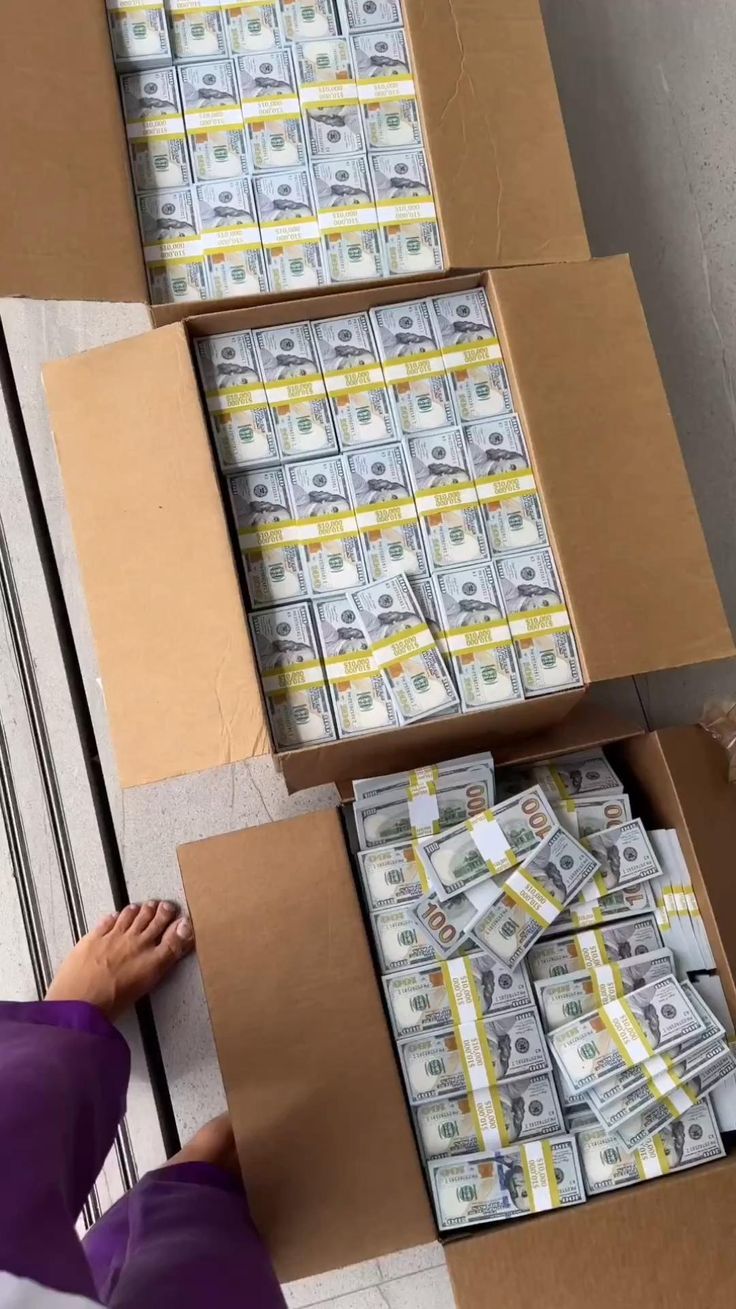 stacks of money are stacked on top of each other in cardboard boxes and being held by a woman