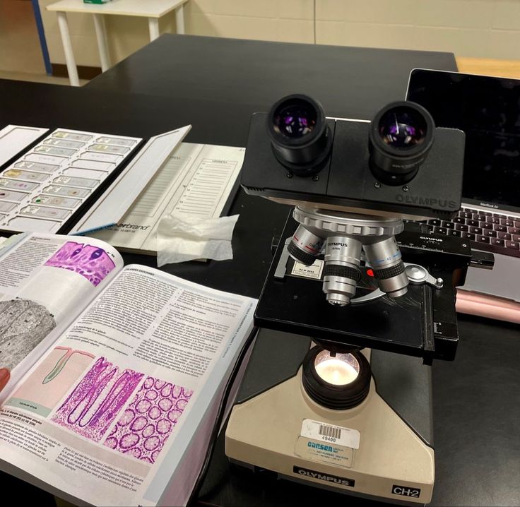 a laptop computer sitting on top of a desk next to a microscope and other items