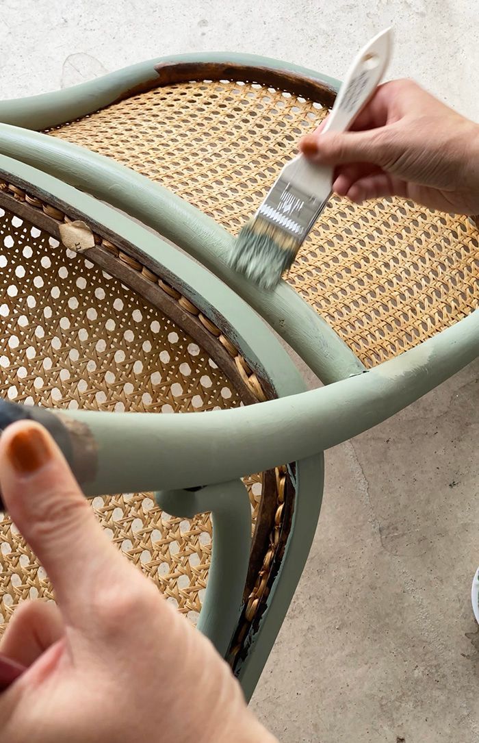 someone using a brush to paint the side of a chair with wicker seats on it