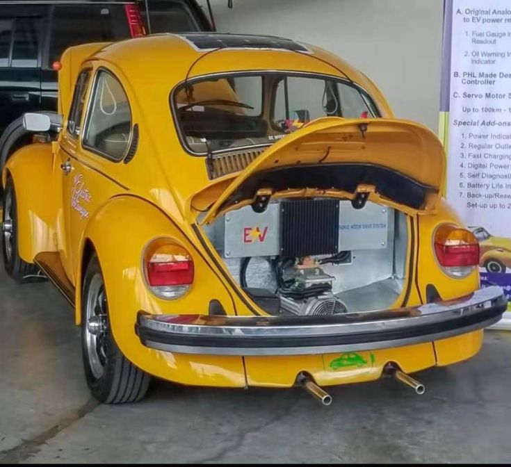 an old yellow vw bug parked in a garage with the hood open and it's engine exposed