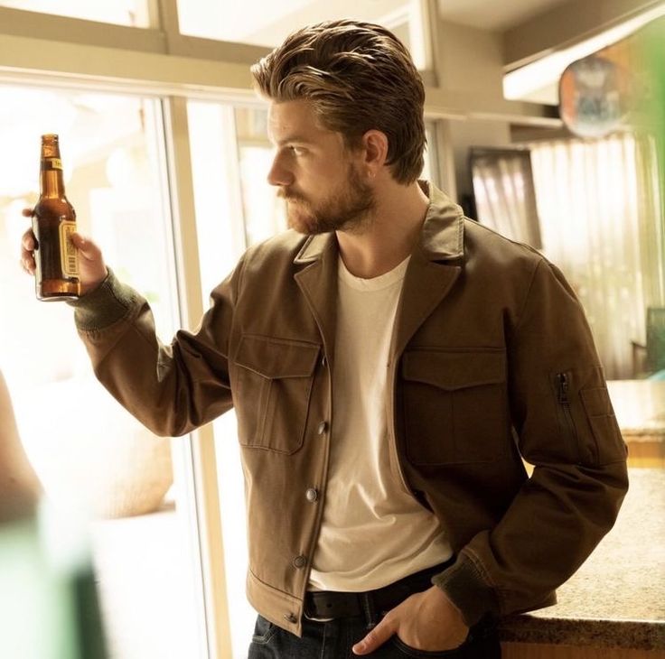 a man standing in front of a window holding a beer