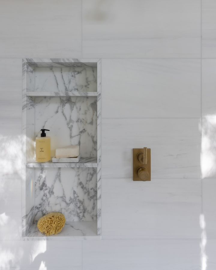 a bathroom with white marble walls and shelves filled with soap, shampoo, and other items