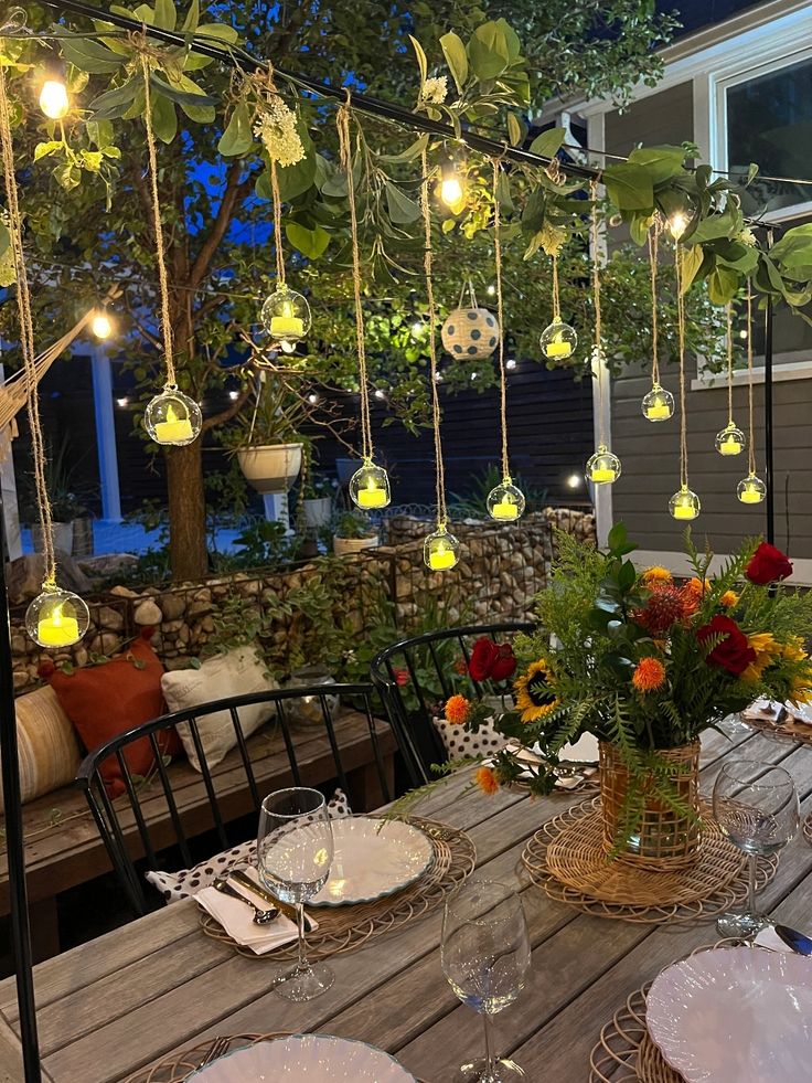 a wooden table topped with lots of plates and glasses next to a tree filled with flowers