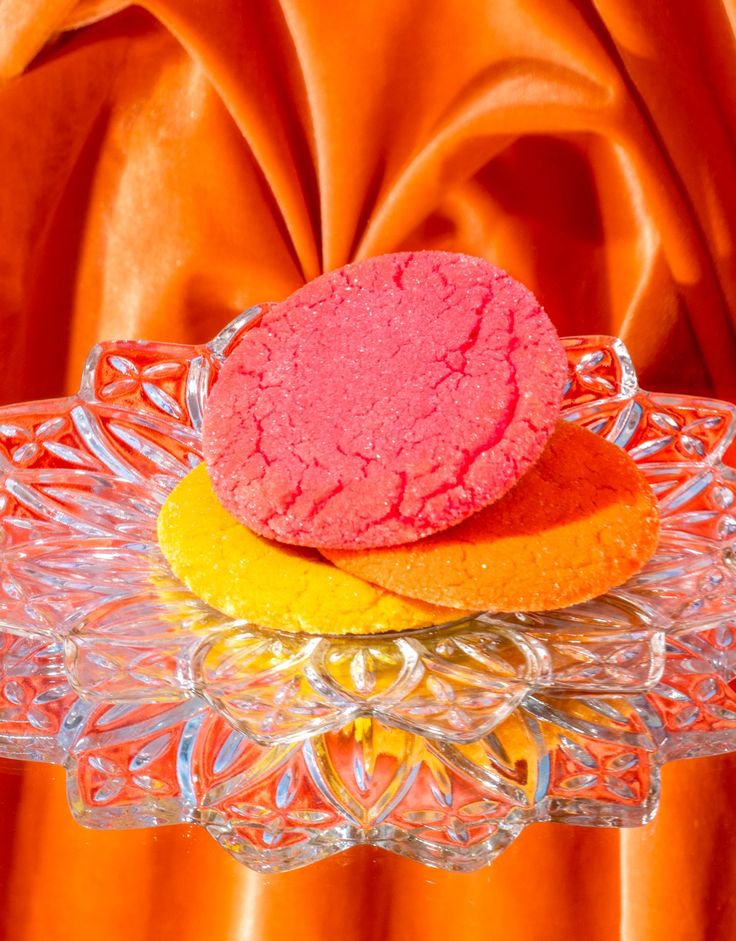 a pink and yellow cookie sitting on top of a glass plate next to an orange cloth