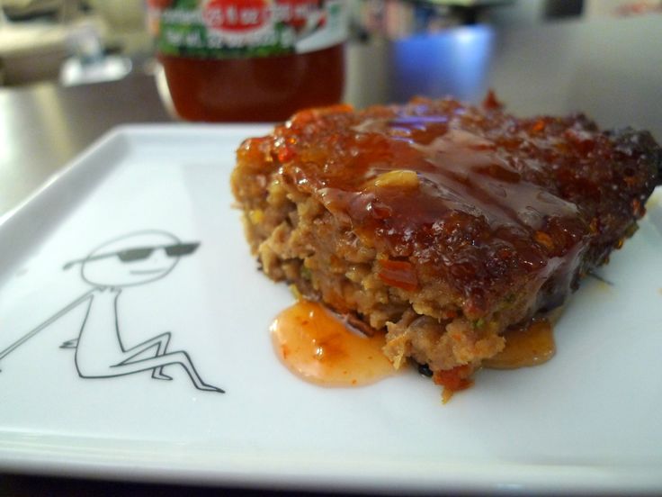 a piece of meatloaf sitting on top of a white plate next to a jar of ketchup