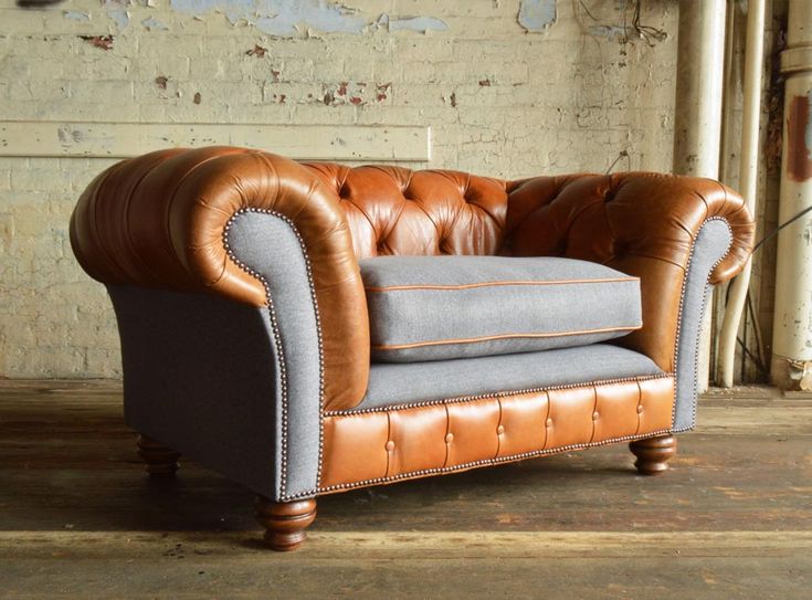 a brown leather chair sitting on top of a wooden floor next to a brick wall