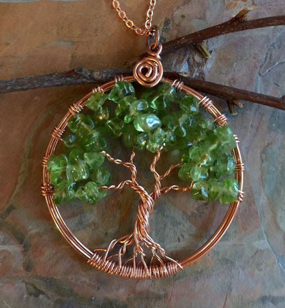 a tree of life pendant with green glass beads on a gold plated chain hanging from a stone wall