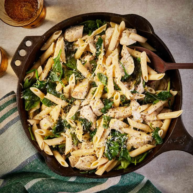 a skillet filled with pasta and spinach covered in chicken, parmesan cheese