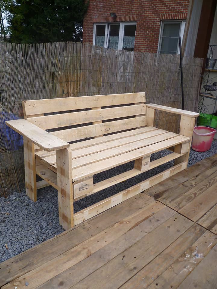 a wooden bench sitting on top of a wooden deck next to a wall and potted plant