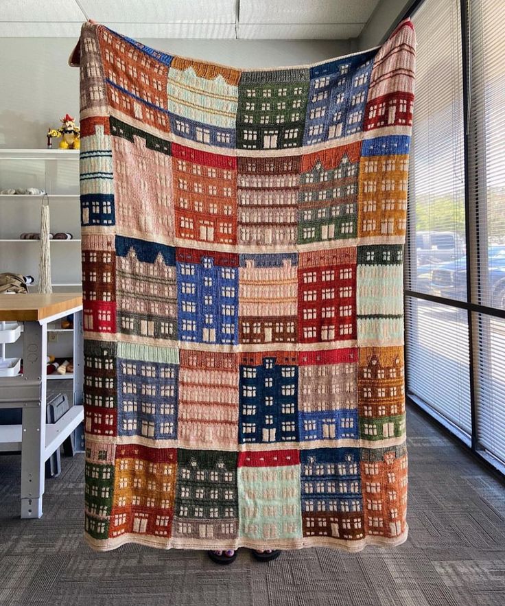 a large multicolored quilt hanging from the ceiling in an office space with windows