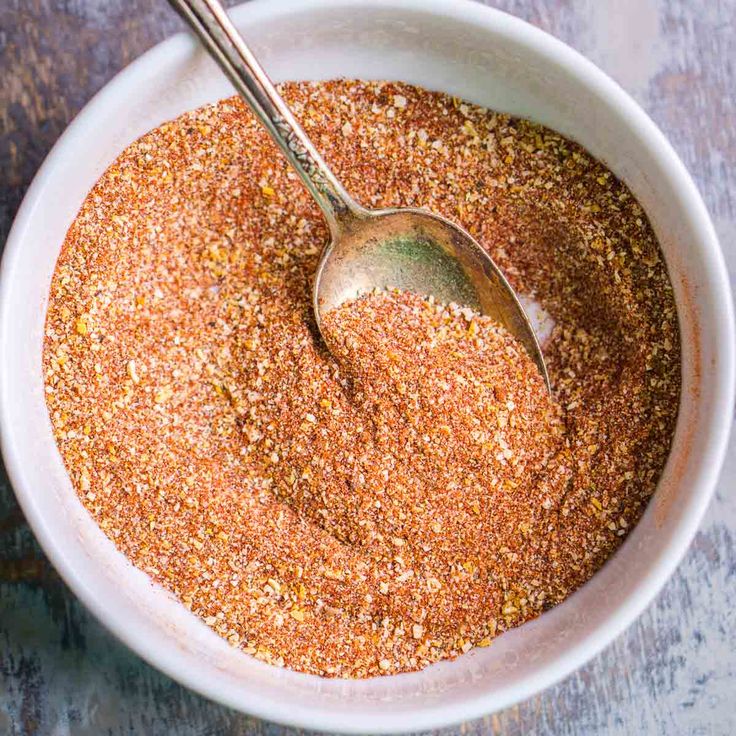 a white bowl filled with spices on top of a wooden table next to a spoon