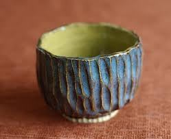 a blue and green vase sitting on top of a red tablecloth covered floor next to a wooden spoon