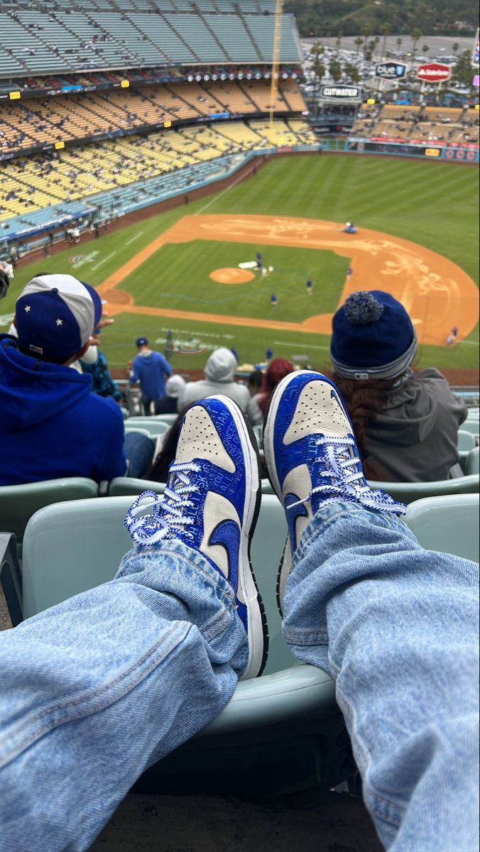 two people sitting in the bleachers at a baseball game with their feet up