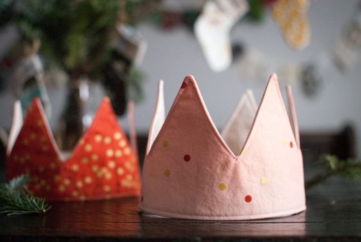 three pink and orange crowns sitting on top of a wooden table next to christmas decorations