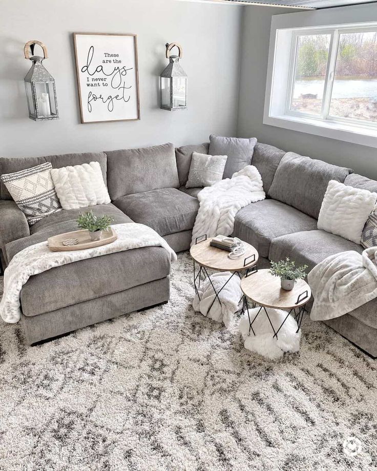 a living room with gray couches and pillows on the floor, two tables in front of them