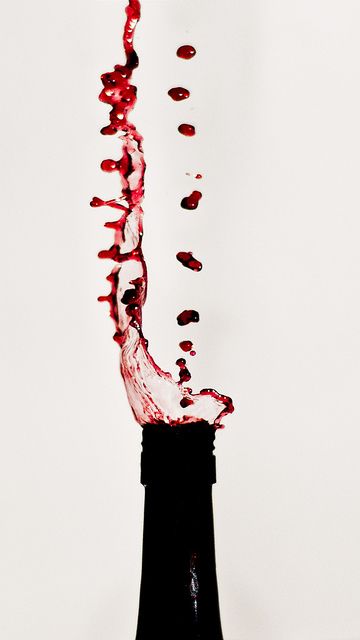 a wine bottle with red liquid pouring out of it's top into the air