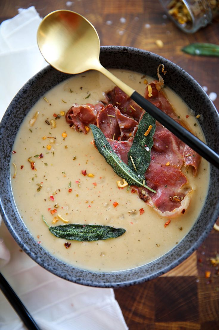 a bowl of soup with meat, cheese and herbs on the side next to two spoons