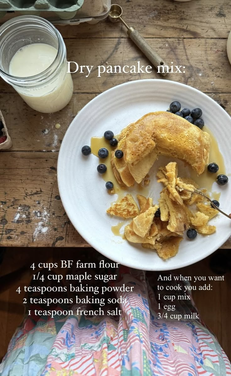 pancakes with blueberries and syrup on a white plate next to a glass of milk