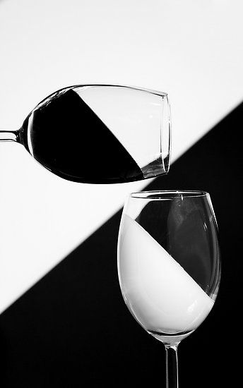 a wine glass with white wine being poured into it, in front of a black and white background