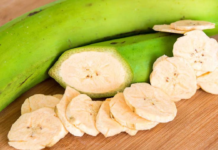 a green banana sitting on top of a wooden table next to cut up pieces of fruit