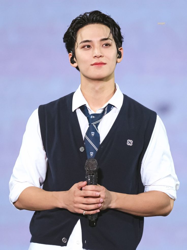 a young man wearing a vest and tie holding a microphone