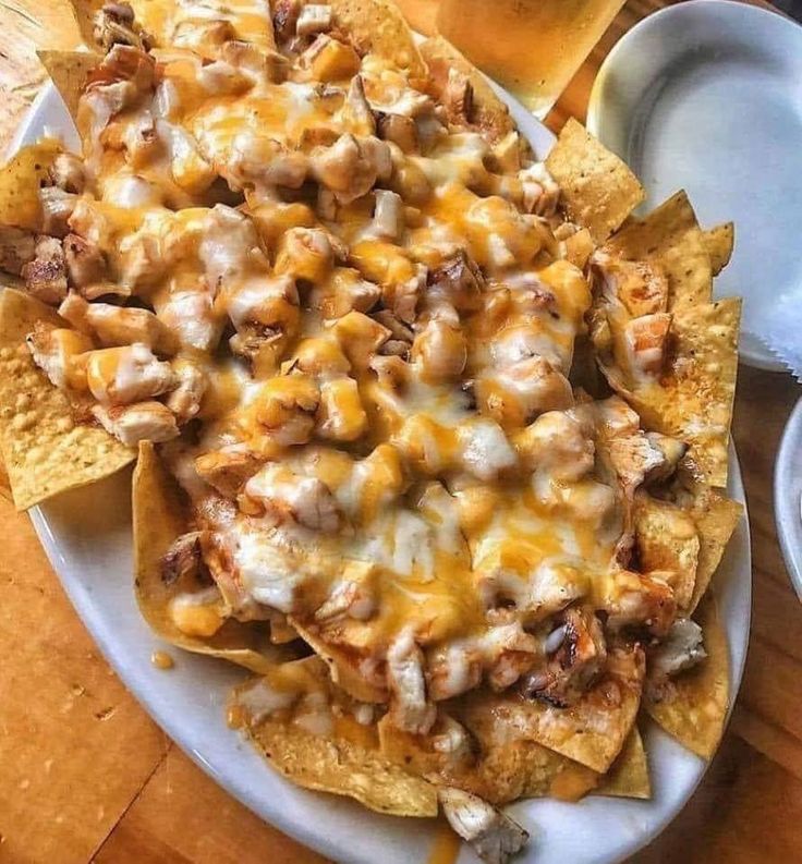 nachos with cheese and meat are served on a plate next to a glass of beer