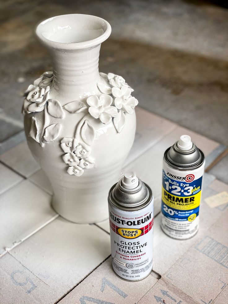 a white vase sitting on top of a tile floor next to spray paint and a can