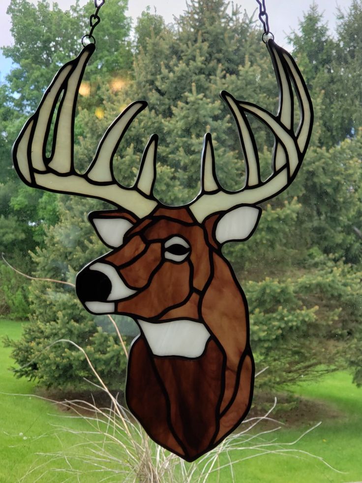 a stained glass deer head hanging from a chain in front of some grass and trees