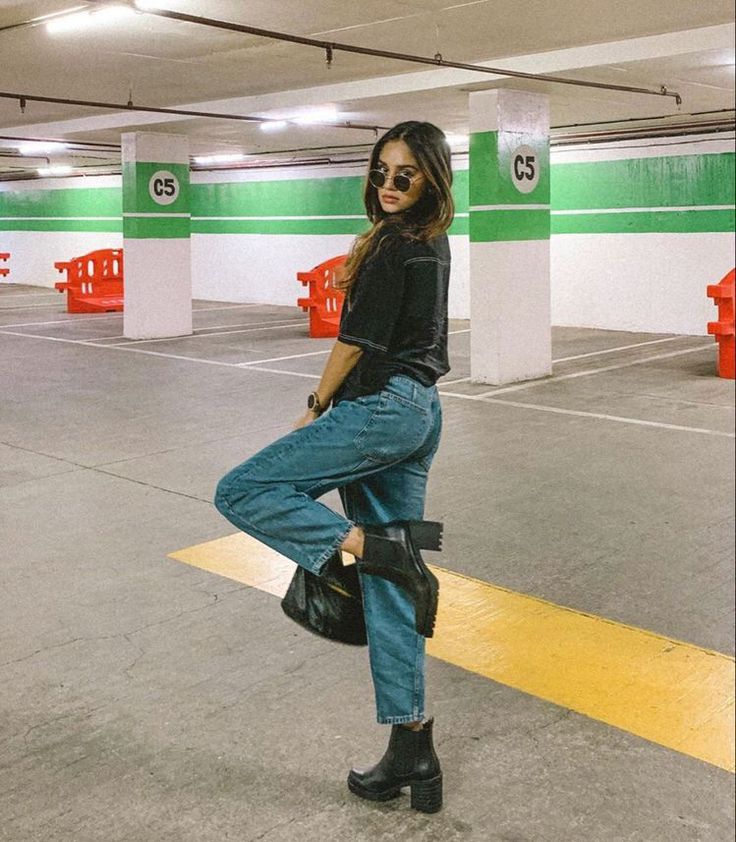 a woman standing in a parking garage with her leg up on the ground and wearing black boots