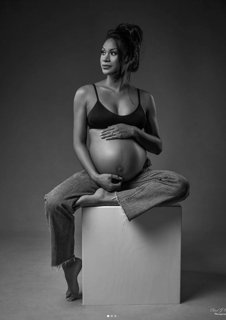 a pregnant woman sitting on top of a white box with her hands in her stomach