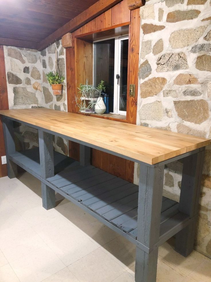 a wooden table sitting in front of a stone wall next to a potted plant