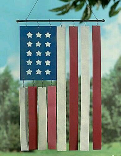 an american flag wind chime hanging from a tree in front of a field with trees